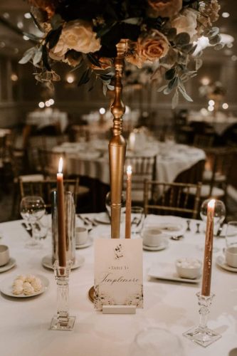 Table name surrounded by candle light under flower arrangement by Rosewater Decor