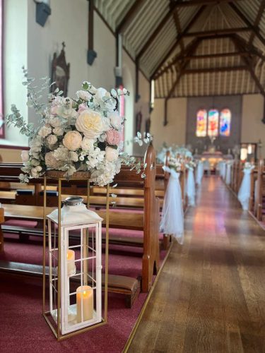 Flower and lantern stand with church aisle in the background by Rosewater Decor