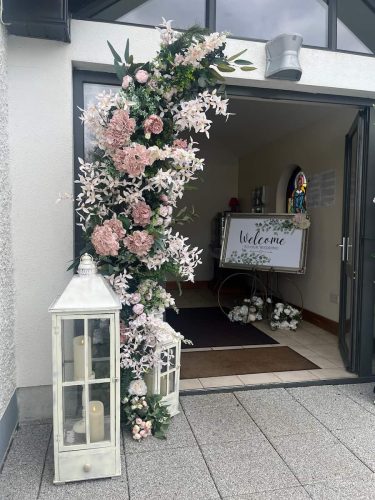Floral arch and lanterns at door of church with welcome sign in the background