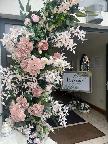 Close up of flower arch at church entrance with welcome sign in background by Rosewater Decor