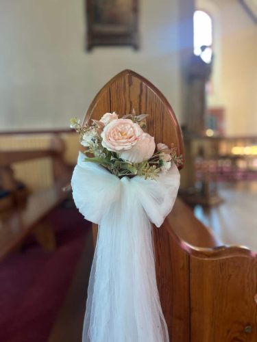 Close up of small bunch of flowers in a white tulle bow on end of pew by Rosewater Decor